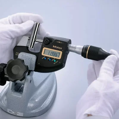 Quality control engineer using a calibrated micrometer to measure exact outer diameter and thread tolerances on a custom brass component.